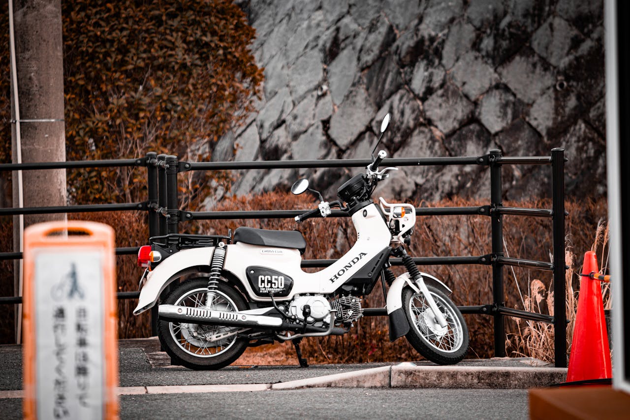 A detailed photograph of a classic white Honda motorcycle parked by a fence in an outdoor setting.